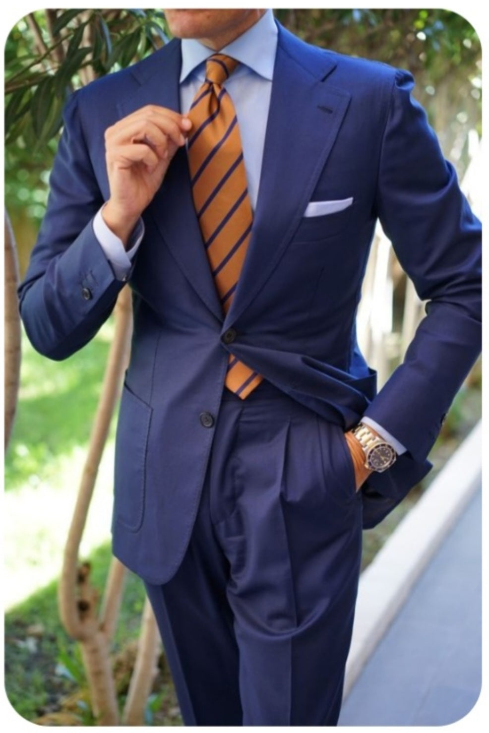 Man wearing a blue suit with an orange striped tie outdoors.