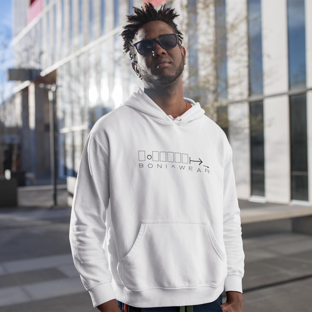 Man wearing a white hoodie with a logo and text, standing outdoors.